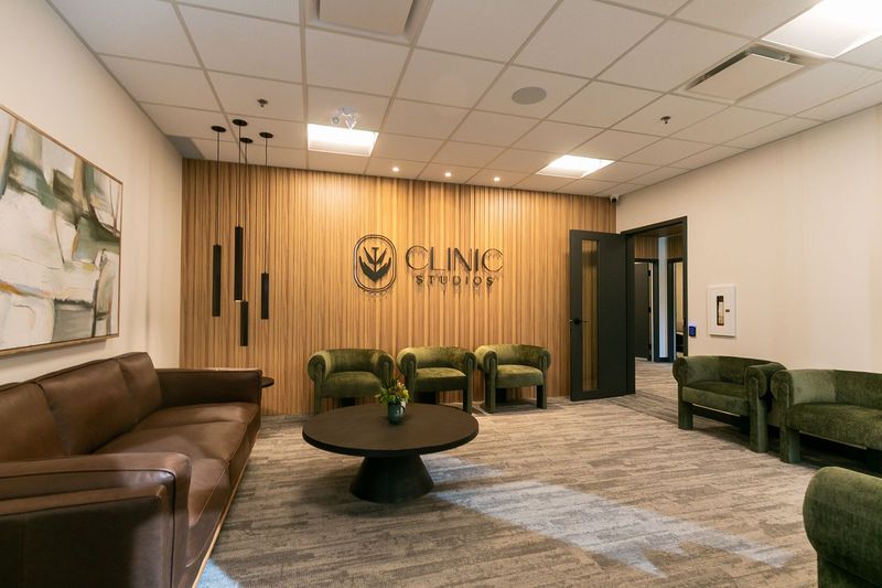 Clinic Studios reception: a wood slat wall with the logo, green velvet chairs, a brown leather sofa and pendant lights